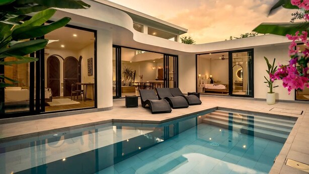 Un área de piscina moderna con sillones de descanso, un espacio habitable con paredes de vidrio y vistas al cielo.