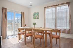 A dining area with a round table, six chairs, a potted plant, and a view of a balcony.