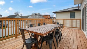 A wooden deck with a table and chairs, a white fence, and houses in the background.