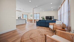 A spacious living area with a blue sofa, a TV, and a dining table.