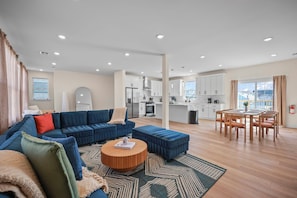 A modern living room with a blue sofa, a wooden coffee table, and a dining area with a wooden table and chairs.