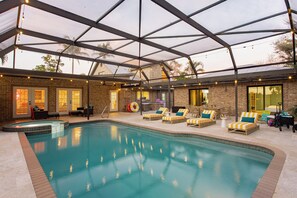 Une piscine intérieure dotée de chaises longues, d’un parasol et d’un mur en briques.