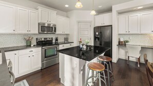 A kitchen with white cabinets, stainless steel appliances, a black refrigerator, and a central island with stools. - Quiet Boise Retreat|Hot Tub•Game Room• 4BR (Boise)