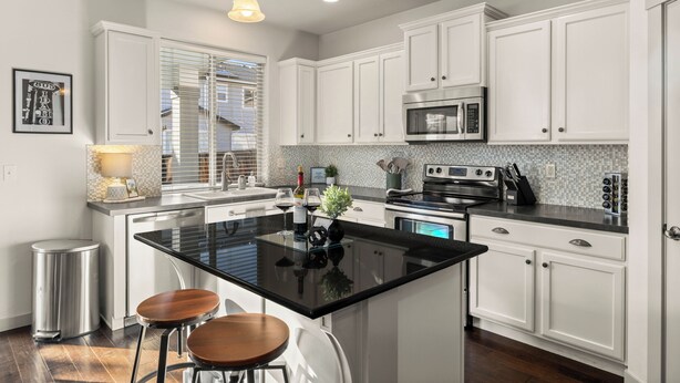 A modern kitchen with white cabinets, a black countertop, stainless steel appliances, and two bar stools. - Quiet Boise Retreat|Hot Tub•Game Room• 4BR (Boise)