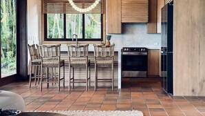 Een moderne keuken met houten kasten, een eethoek met rieten stoelen en een groot raam met uitzicht op groen.