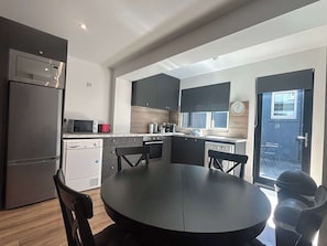 A compact kitchen with modern appliances, a dining area with a round table, and a view through a glass door.