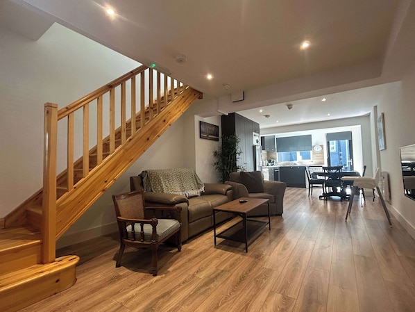 A modern living room with a wooden staircase, a sofa, a coffee table, and a dining area with chairs and a table.