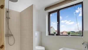 A bathroom with a shower, toilet, bathtub, and a window with a view of buildings. - 4 Star Holiday Home in Lokken (Lokken)