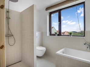 Ein Badezimmer mit Dusche, Toilette, Badewanne und einem Fenster mit Blick auf Gebäude.