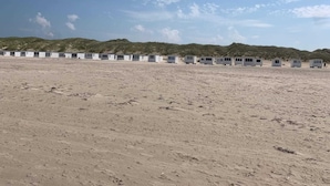 A row of small, white, single-story mobile homes on a sandy beach with hills in the background. - 4 Star Holiday Home in Lokken (Lokken)