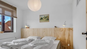 A bedroom with a bed, a wooden headboard, a hanging light fixture, a window with blinds, and a small stool. - 4 Star Holiday Home in Lokken (Lokken)