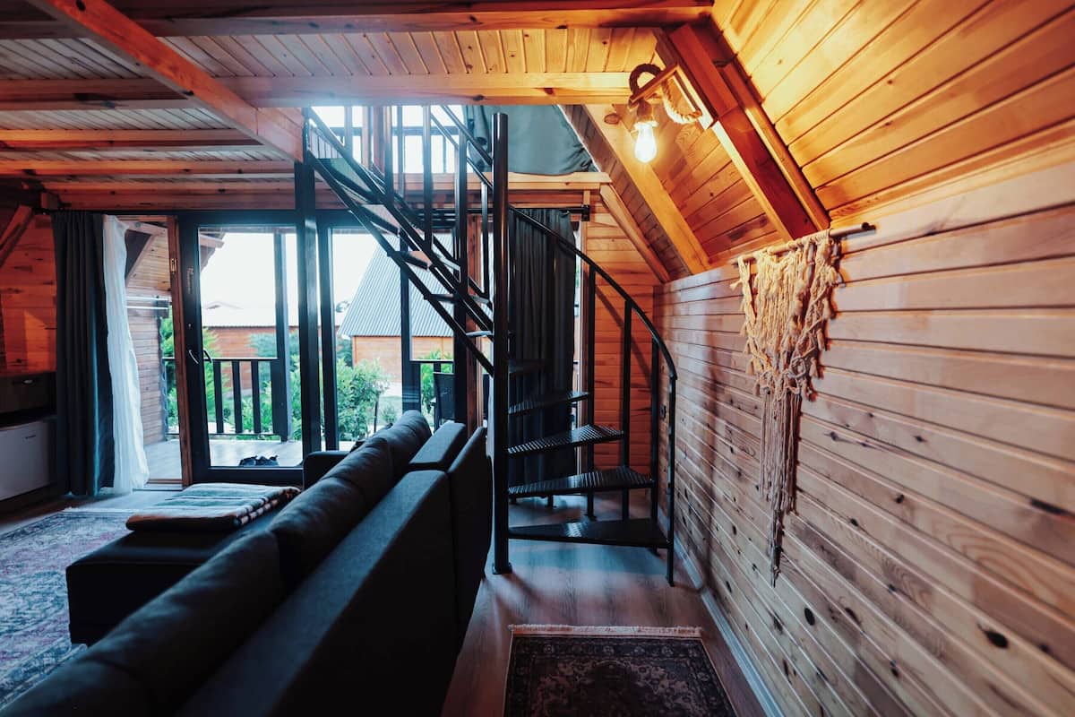 Een houten interieur met een trap, een bank en uitzicht door een glazen deur.