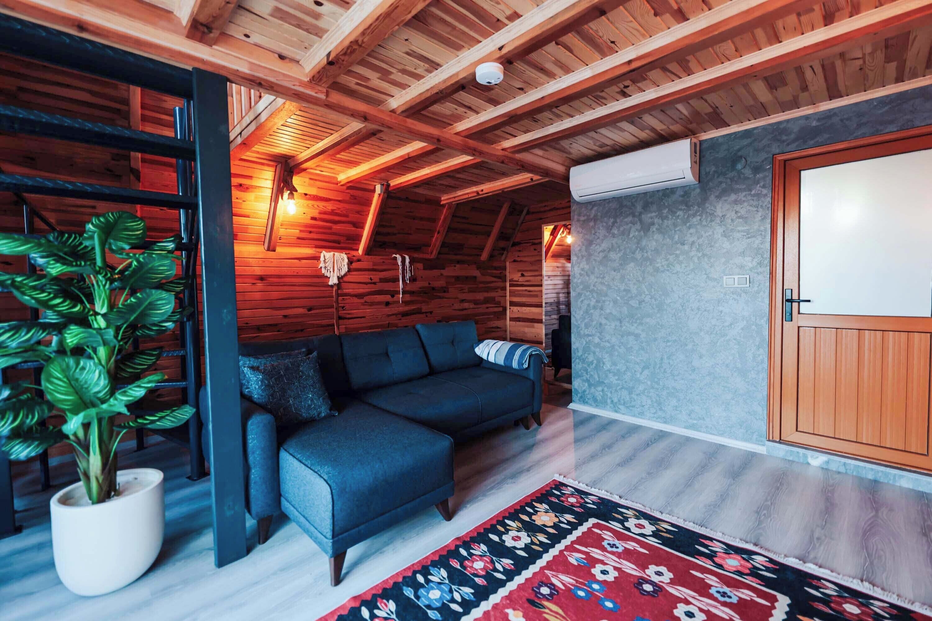 A cozy room with a dark blue sofa, a wooden ceiling, and a large window.