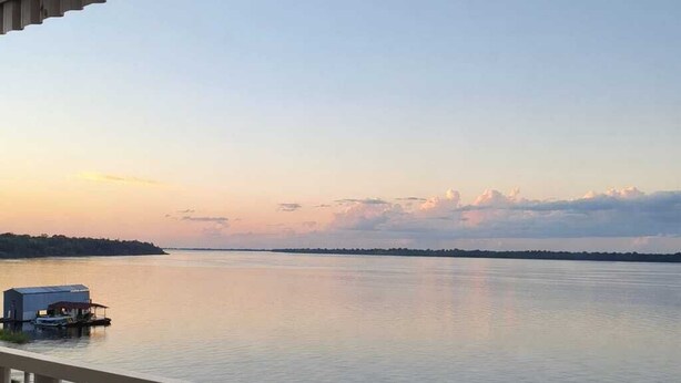 Un balcón con vista a un cuerpo de agua tranquilo y una costa distante al atardecer.