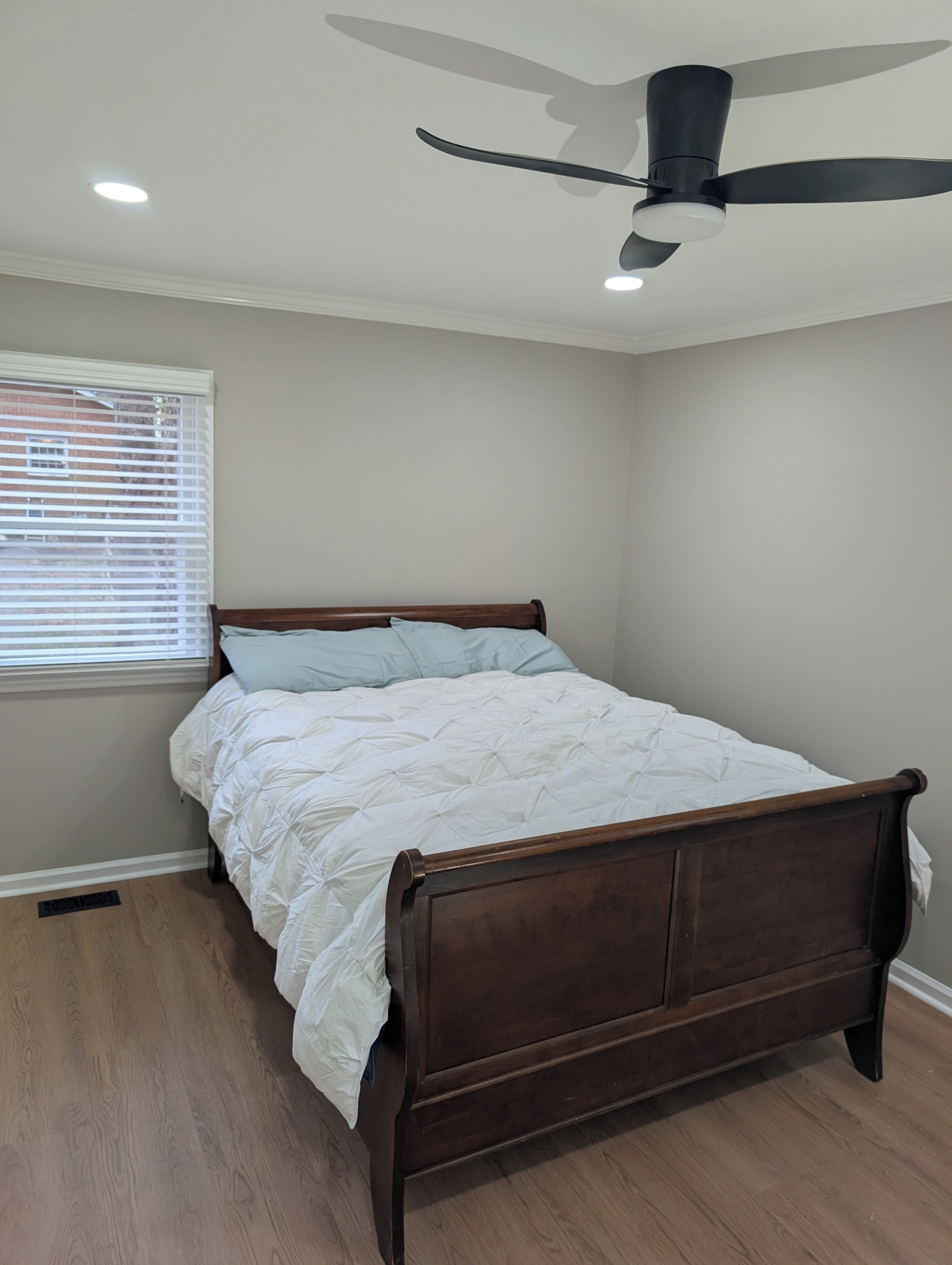 A bedroom with a wooden bed, a ceiling fan, and a window with blinds.