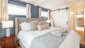 Ein Schlafzimmer mit Bett, Kissen, einem Nachttisch, einer Lampe und Blick ins Badezimmer.