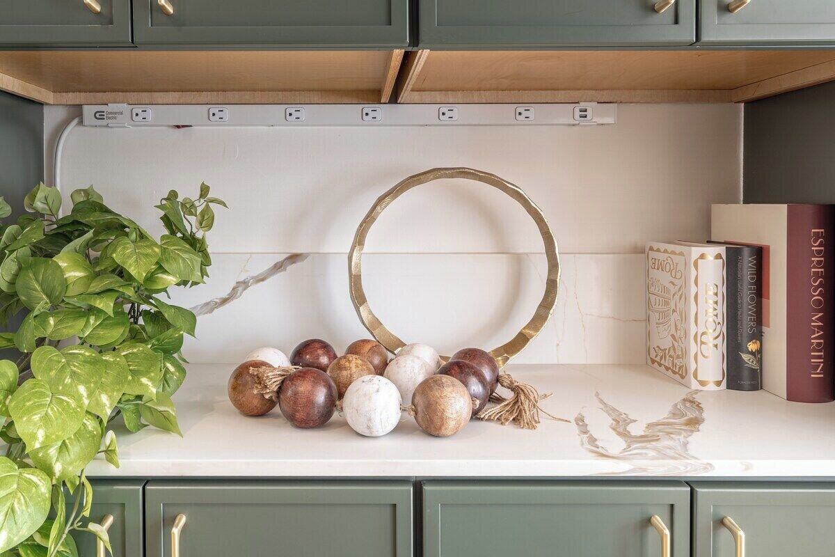 Uma bancada de cozinha com uma composição decorativa de frutas e um anel dourado, uma planta em vaso e livros.