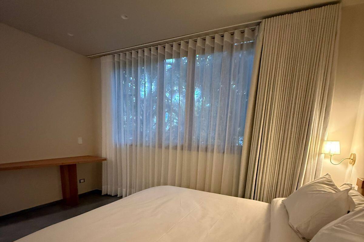 Una habitación de hotel con una cama grande, un escritorio, una lámpara y una ventana con cortinas.
