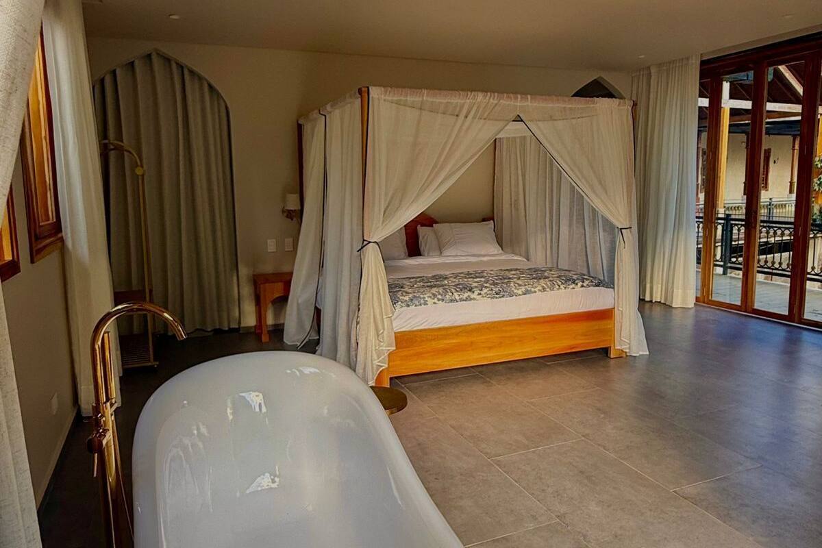 Un dormitorio con cama con dosel, una bañera y un ventanal grande.