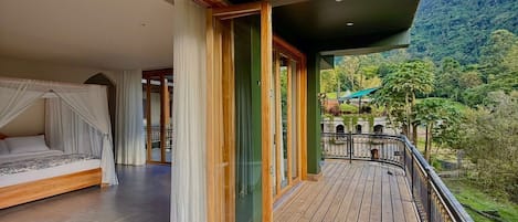 A wooden deck with a bed and curtains, a glass door, and a view of a mountainous landscape.