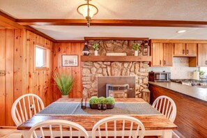 Un intérieur en bois avec une cheminée en pierre, une table à manger avec des chaises et un coin cuisine.