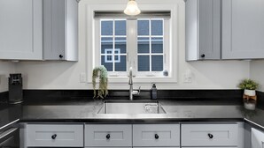 Una cucina moderna con mobili grigi, un piano di lavoro nero, un lavello in acciaio inossidabile e un lampadario a sospensione.