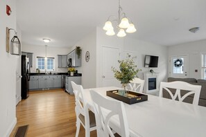 A modern kitchen with grey cabinets, a black refrigerator, and a dining area with white chairs and a table. - Weirs Beach Retreat | Pool | Near Winnipesaukee (Laconia)
