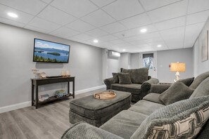 A living room with grey sofas, a dark wooden side table, and a flat-screen TV mounted on the wall. - Weirs Beach Retreat | Pool | Near Winnipesaukee (Laconia)