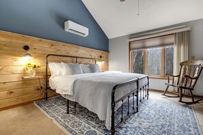 Ein Schlafzimmer mit einem Bett, einem Schaukelstuhl, einem Fenster mit Vorhängen, einer Wand-Klimaanlage und einem Holzkopfstück.