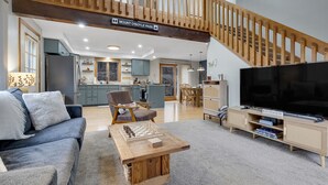 En moderne stue med en trappe i træ, en sofa, et sofabord med skakbrikker og et fjernsyn.