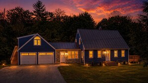 Une maison à deux étages avec un garage, un porche à l’avant et une allée bien éclairée.