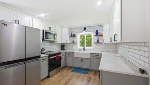 Une cuisine moderne dotée d’appareils électroménagers en acier inoxydable, de meubles blancs, d’un four à micro-ondes et d’une fenêtre laissant entrer la lumière naturelle.