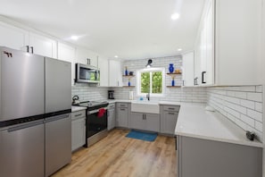Une cuisine moderne avec des meubles blancs, des appareils en acier inoxydable, un four à micro-ondes et une fenêtre donnant sur un beau paysage.