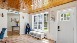 Une pièce avec un plafond en bois, une porte blanche, une grande fenêtre, une bibliothèque bleue et un banc.