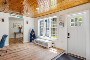 Une pièce avec un plafond en bois, une porte blanche, une grande fenêtre, une bibliothèque bleue et un banc.