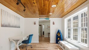 Habitació amb sostre de fusta, un escriptori amb cadira, una finestra amb persianes i una estanteria blava amb un vas.