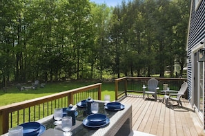 A wooden deck with a table set for dining, surrounded by trees.