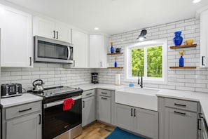 A modern kitchen with white cabinets, a microwave, a stove, and a window with a view of greenery.