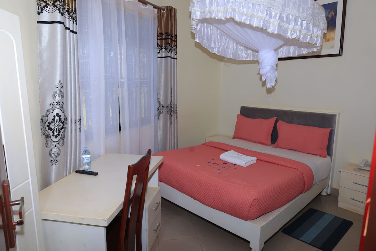 A bedroom with a bed, a desk, a chair, a nightstand, and a hanging canopy.