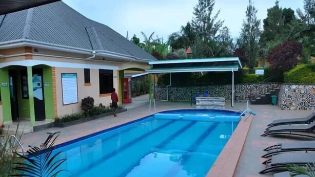 A swimming pool with a covered area, lounge chairs, and a building with a green facade.