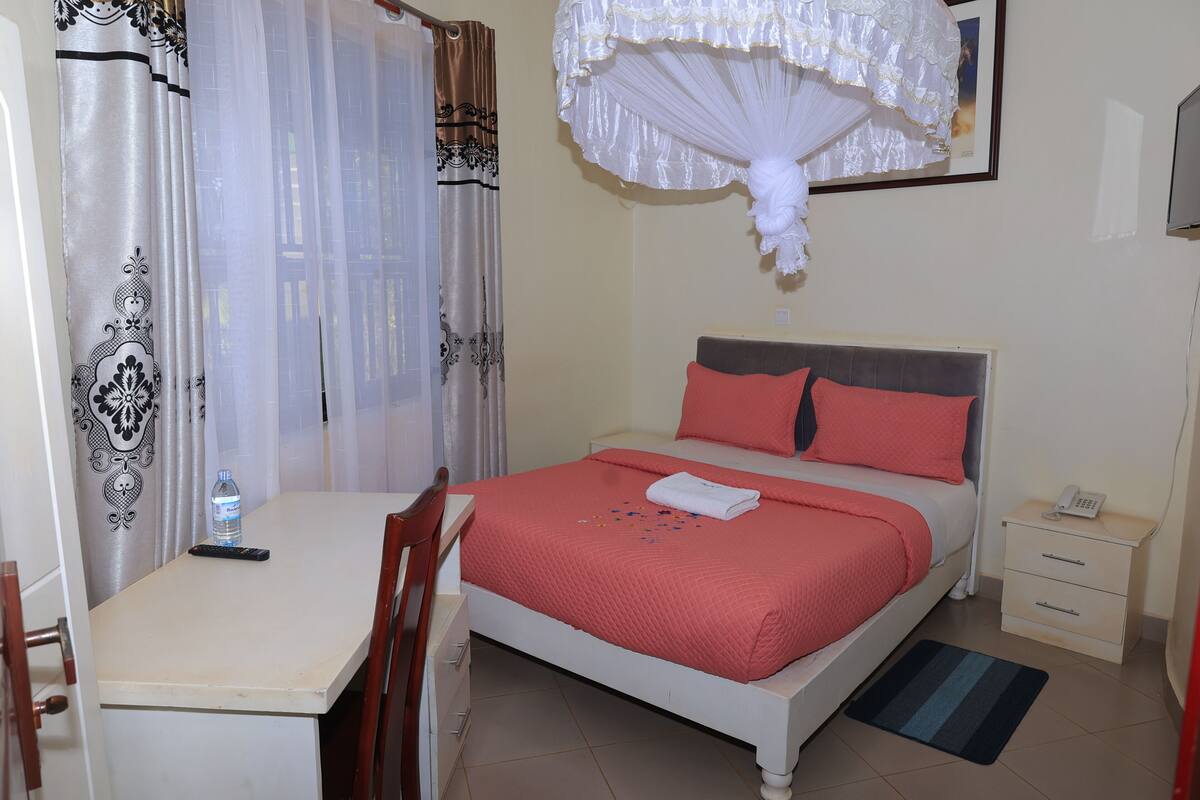 A bedroom with a bed, bedside table, chair, and a desk with a chair.