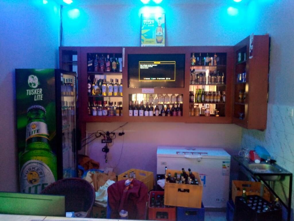 A bar area with shelves of bottles, a refrigerator, and a television screen.