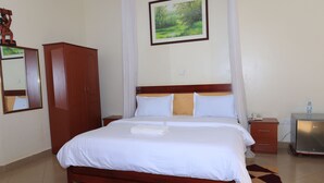 A neatly made bed with white linens, a wooden headboard, a nightstand with a lamp, a wardrobe, and a framed picture on the wall.