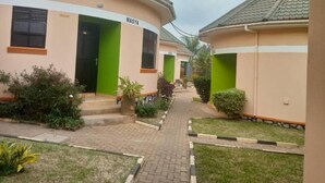 A corridor with houses labeled 'MASYA' and 'MASYA,' featuring a paved walkway, green doors, and potted plants.