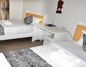 A hotel room with two beds, a desk, a telephone, and a decorative wall piece. - Lorycon Hotel Rukungiri  (Rukungiri)