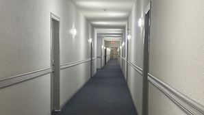 A long, narrow hotel corridor with doors on both sides, carpeted floors, and wall-mounted light fixtures. - CozyVibe - King Bed. (Edmonton)