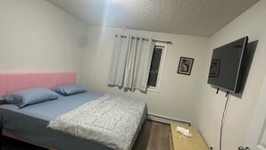 A bedroom with a bed, a bedside table, a TV mounted on the wall, and a window with curtains. - CozyVibe - King Bed. (Edmonton)