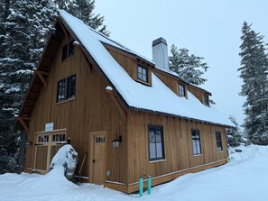 A wooden cabin with a steeply pitched roof, large windows, and a chimney.