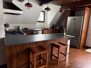 A modern kitchen with a large island, wooden bar stools, stainless steel appliances, and pendant lighting.