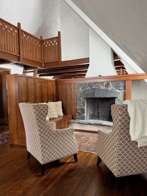 A loft-style room with a stone fireplace, wooden paneling, and patterned armchairs.
